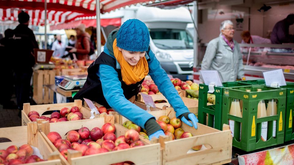 20.03.2020, Niedersachsen, Hannover: Verkäuferin Charleen Wagner vom Obsthof Busch entnimmt auf dem Wochenmarkt am Stephansplatz Äpfel aus einer Kiste, um sie zu wiegen. Um die Versorgung der Bevölkerung sicherzustellen, finden Wochenmärkte weiterhin st... Eine Obsthändlerin auf einem Wochenmarkt