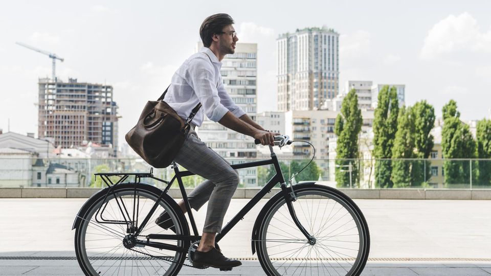 HIGH-RES: side view of young man in stylish clothes riding vintage bicycle on city street Ein Mann auf einem Rad