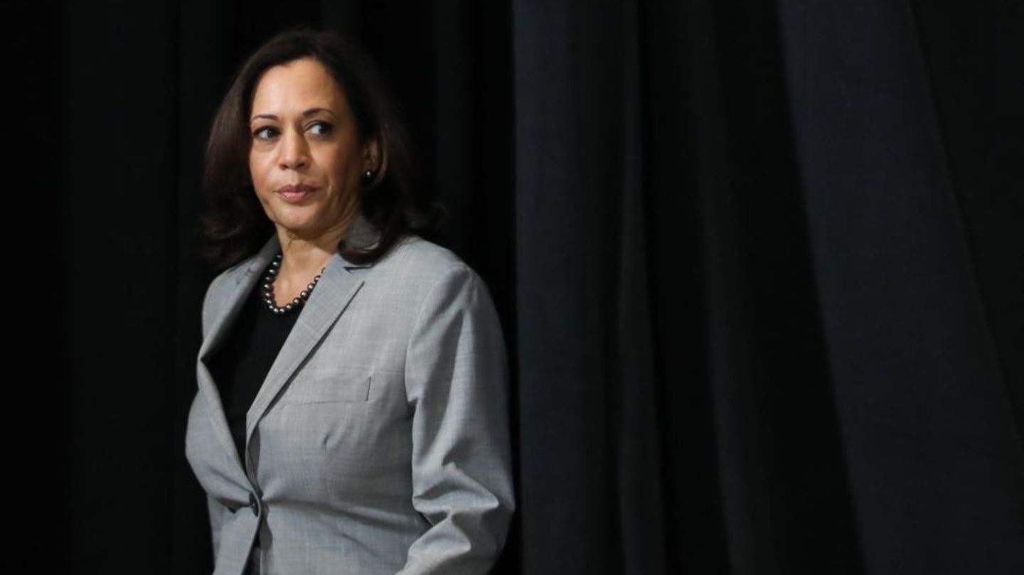 Kamala Harris tritt vor einem dunklen Vorhang auf eine Bühne