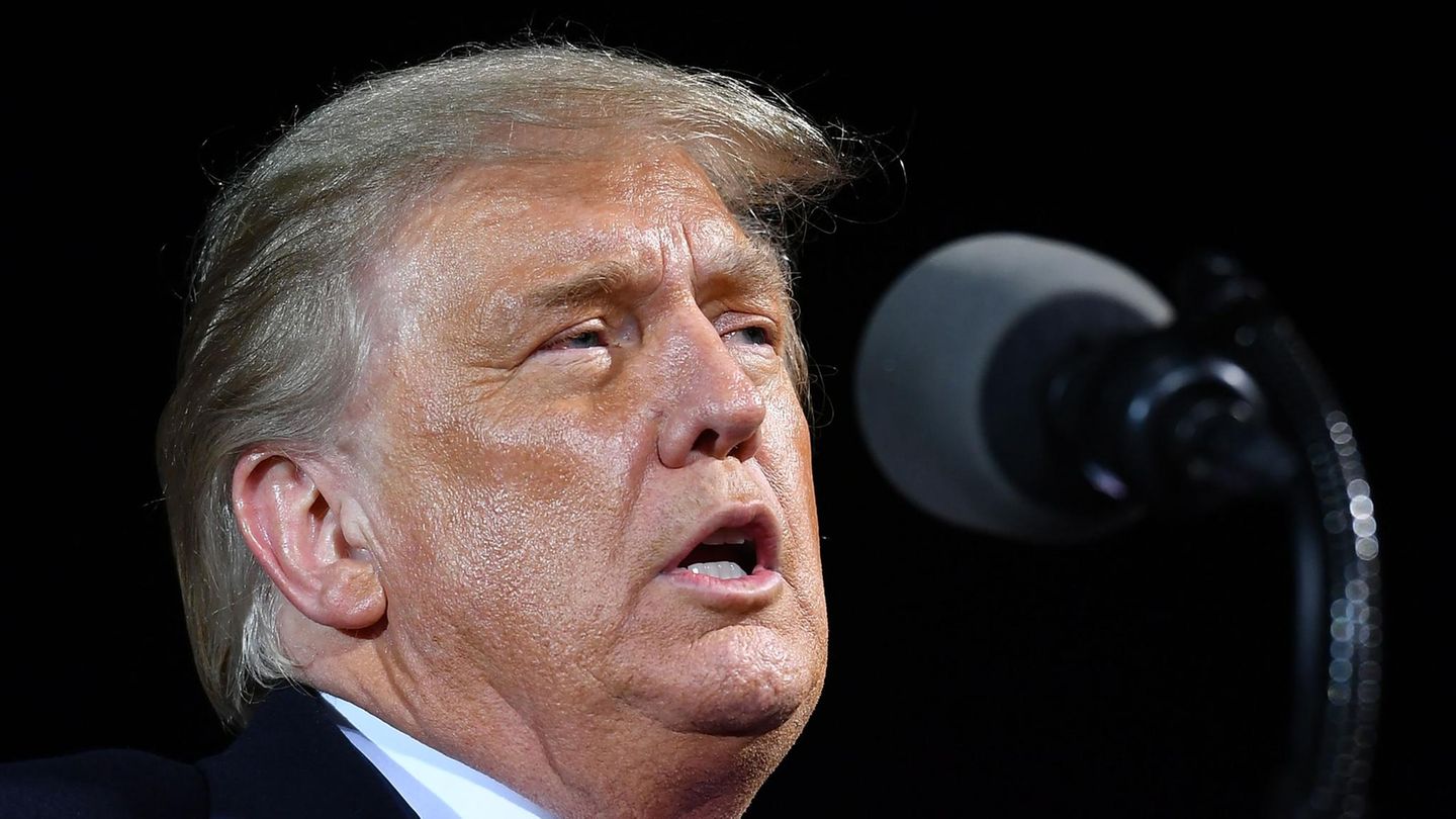 US-Präsident Donald Trump steht hell angeleuchtet in einer Halle und spricht in ein Mikrofon