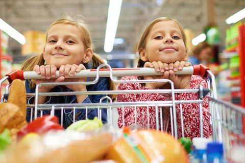 Zwei Mädchen umklammern einen Griff am Einkaufswagen