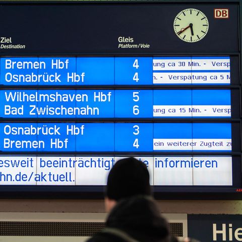 Verspätungen: Reisende stehen am Morgen am Bahnhof und schauen zur Anzeigetafel der Deutschen Bahn: