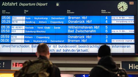 Verspätungen: Reisende stehen am Morgen am Bahnhof und schauen zur Anzeigetafel der Deutschen Bahn:
