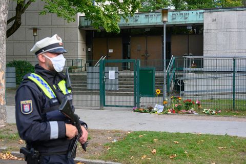 Ein Polizist steht vor der Synagoge in Hamburg, vor der ein jüdischer Student angegriffen wurde. Vor dem Tor liegen Blumen.