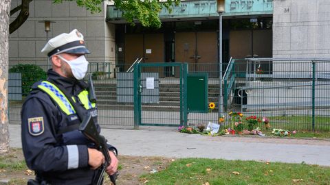 Ein Polizist steht vor der Synagoge in Hamburg, vor der ein jüdischer Student angegriffen wurde. Vor dem Tor liegen Blumen.