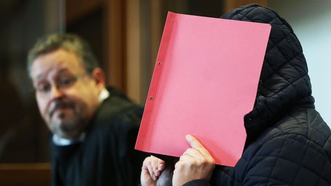 Landgericht Köln: Der Angeklagte verdeckt sein Gesicht mit einem roten Umschlag