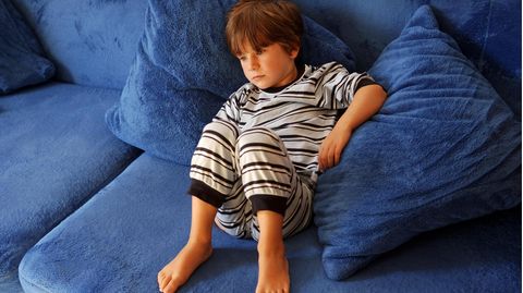 Junge im Schlafanzug liegt auf dem Sofa