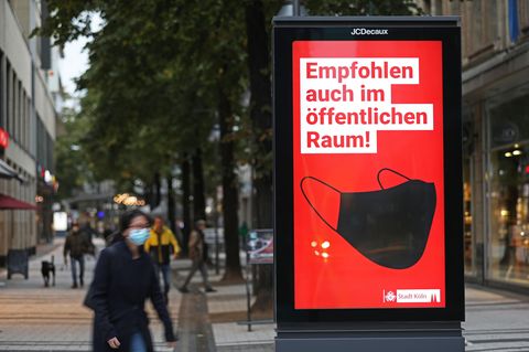 Passanten gehen an einer Werbetafel für das Tragen von Masken vorbei