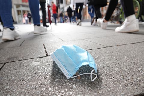 In der Fußgängerzone der Kölner Innenstadt gehen viele Menschen an einer auf dem Boden liegenden Mund-Nasen-Bedeckung vorbei