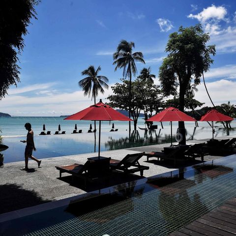 An einem Infinity-Pool stehen liegen unter roten Sonnenschirmen. Doch keine Touristen liegen in der Sonne. Im Hintergrund Palmen