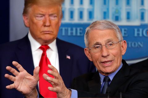 Während Anthony Fauci - mit Brille und weißem Seitenscheitel - am Rednerpult gestikuliert, steht Trump mürrisch schräg dahinter