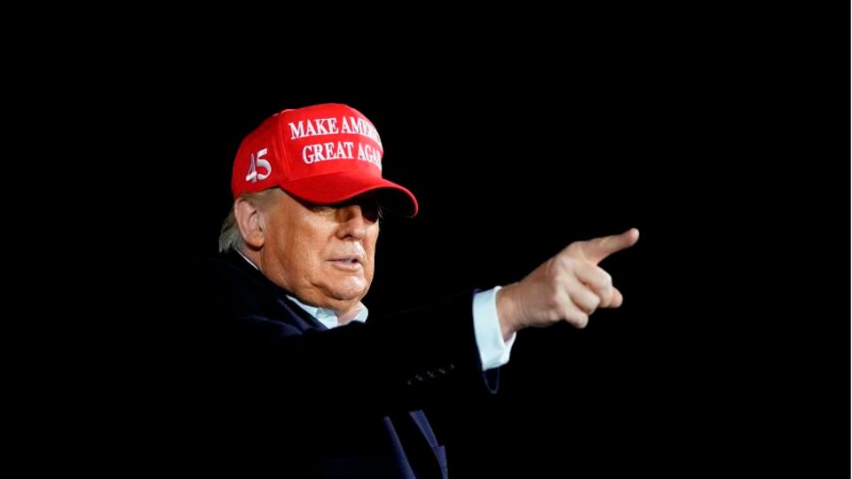 Präsident Trump trägt rote MAGA Cap und deutet mit dem Zeigefinger.