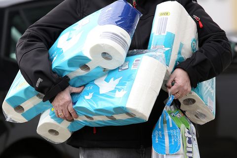 Ein Mann hat den ganzen Arm voller Packungen Toilettenpapier