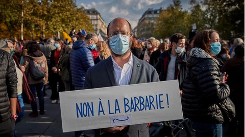 Ein Mann steht mit einem Pappschild "Non à la barbarie" auf einer Demo in Paris