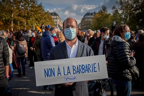 Ein Mann steht mit einem Pappschild "Non à la barbarie" auf einer Demo in Paris