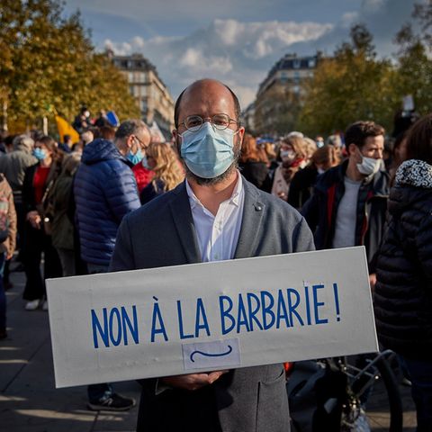 Ein Mann steht mit einem Pappschild "Non à la barbarie" auf einer Demo in Paris
