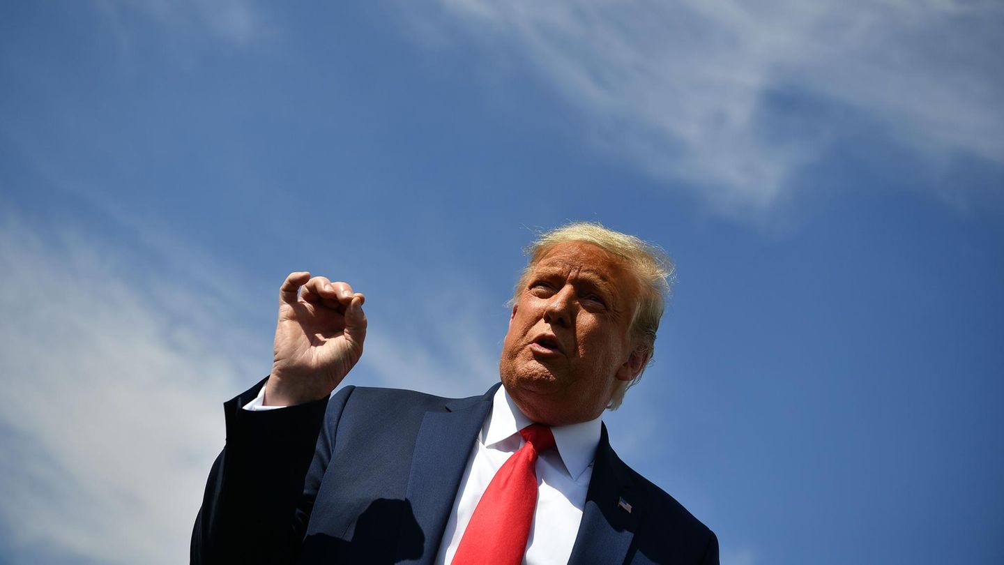 Unter einem blauen Himmel steht US-Präsident Trump an einem Rednerpult und gestikuliert mit der rechten Hand