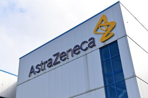 An einer weißen Wellblech-Fabrikhalle hängt der Schriftzug "AstraZeneca", daneben ein gelbes Logo aus stilisierten Buchstaben