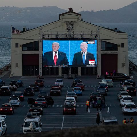 Autos stehen vor eine Leinwand, auf der Trump und Biden gezeigt werden