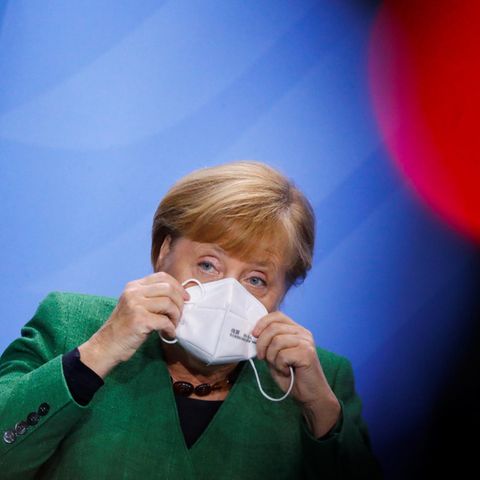 Angela Merkel setzt sich eine Maske auf