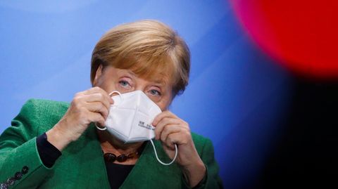 Angela Merkel setzt sich eine Maske auf