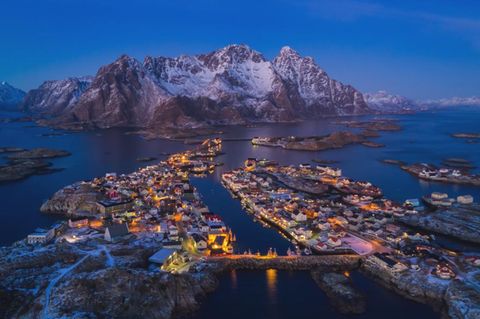 Norwegen, Lofoten: Henningsvær  Im Schein des Mondes leuchten die roten Fischerhäuser und die gelblichen Felsen in warmen Tonen, während der umgebende Ozean ein tiefes Blau annimmt. 