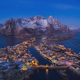Norwegen, Lofoten: Henningsvær  Im Schein des Mondes leuchten die roten Fischerhäuser und die gelblichen Felsen in warmen Tonen, während der umgebende Ozean ein tiefes Blau annimmt. 