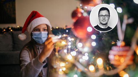 Ein Mädchen mit Maske schmückt den Weihnachtsbaum