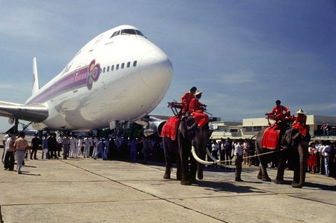Bild 1 von 12 der Fotostrecke zum Klicken:  Begrüßung im Jahre 1979 auf Thailändisch, indem die erste Boeing 747 in der Flotte von Thai Airways von zwei Elefanten über das Rollfeld gezogen wird..