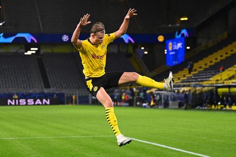 Im gelben BVB-Trikot und schwarzer Hose springt Erling Haaland mit ausgestreckten Armen und Beinen über den Rasen
