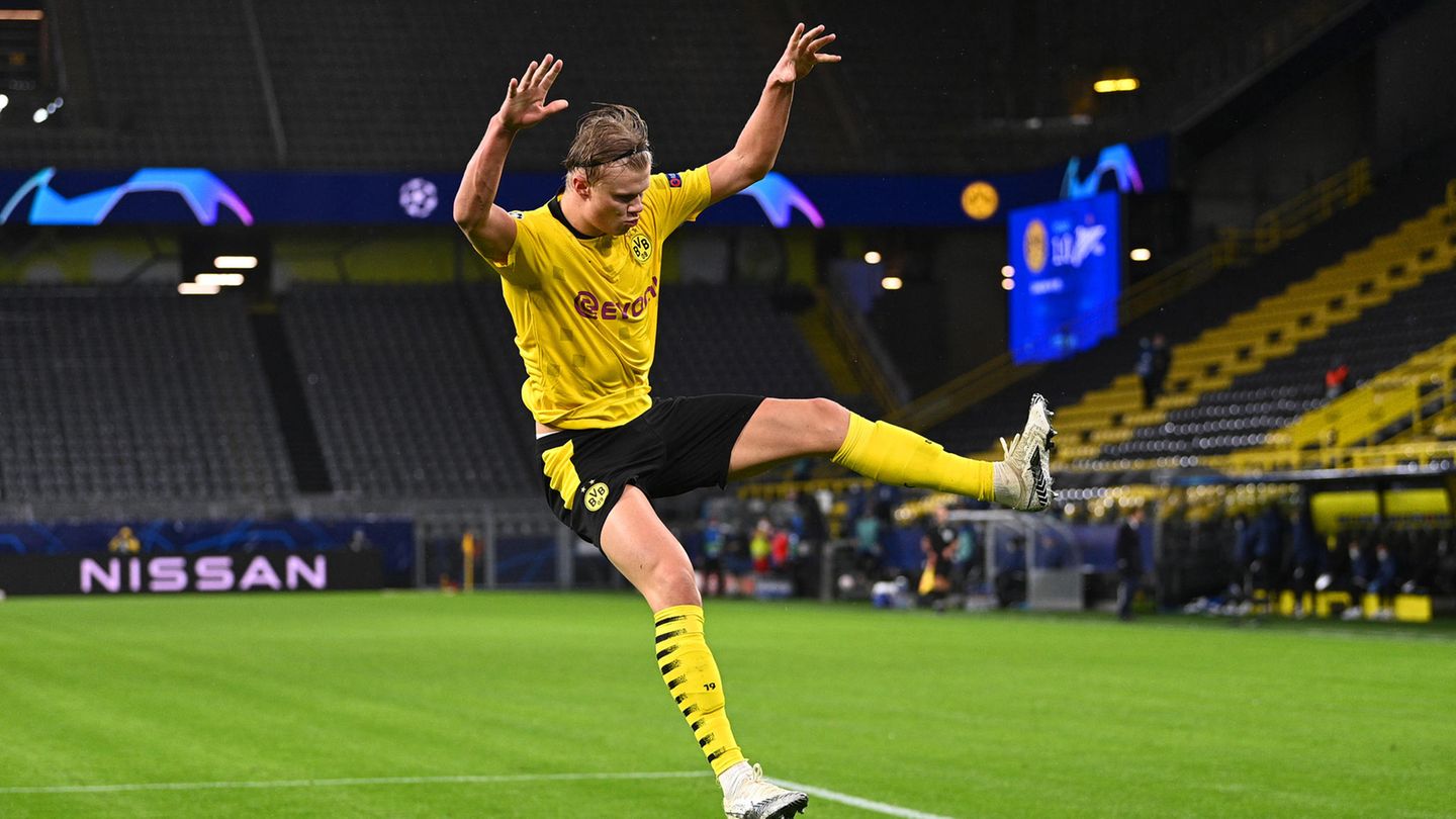 In the yellow BVB Jersey and black pants Erling Haaland jumps with outstretched arms and legs across the lawn