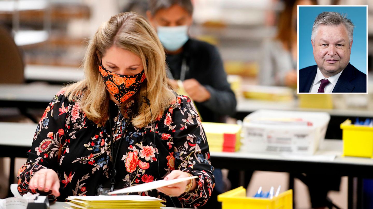 US-Wahl Briefwahl Eine blonde Frau mit Mundschutz und geblümter Bluse sitzt an einem Tisch und sortiert Briefwahl-Unterlagen