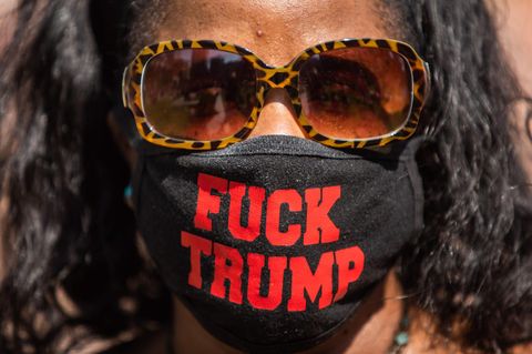 Eine schwarze Frau mit Sonnenbrille trägt einen Mund-Nasen-Schutz mit "FUCK TRUMP"-Schriftzug