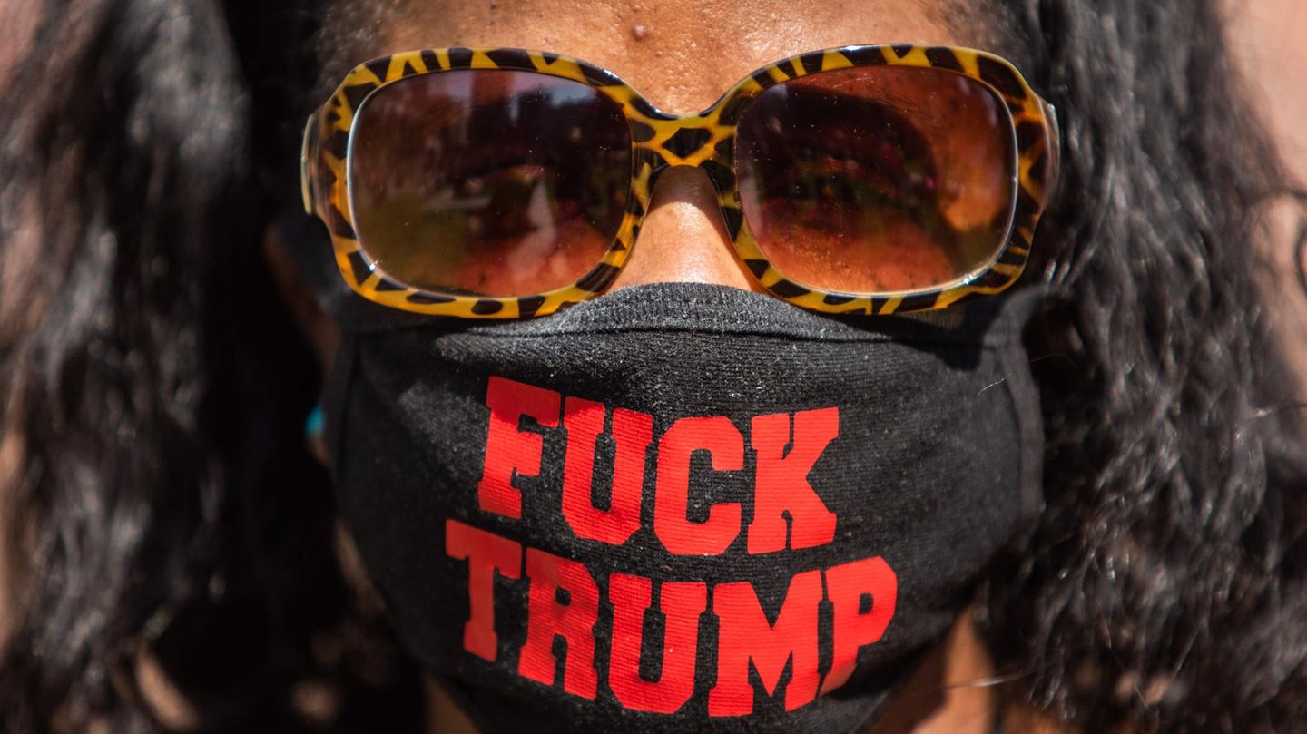 Eine schwarze Frau mit Sonnenbrille trägt einen Mund-Nasen-Schutz mit "FUCK TRUMP"-Schriftzug