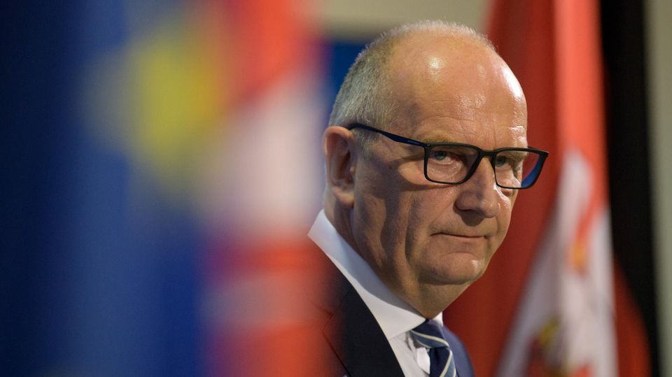 Brandenburgs MP Dietmar Woidke schaut ernst zwischen Flaggen hervor