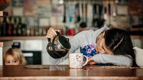 Eine müde Mutter schenkt sich Kaffee ein und verfehlt die Tasse