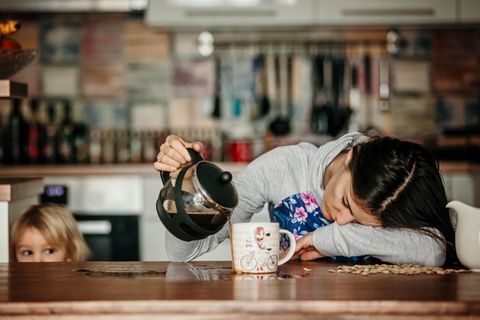 Eine müde Mutter schenkt sich Kaffee ein und verfehlt die Tasse