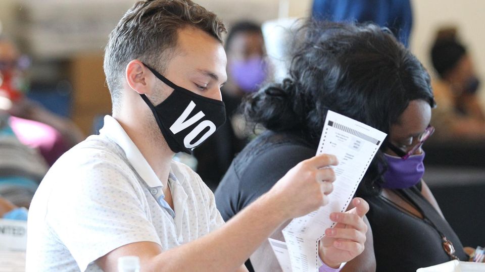 US-Wahl Auszählung Atlanta Georgia Ein junger weißer Mann und eine übergewichtige schwarze Frau sitzen nebeneinander und halten Wahlzettel in den Händen