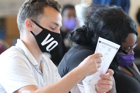 Ein junger weißer Mann und eine übergewichtige schwarze Frau sitzen nebeneinander und halten Wahlzettel in den Händen