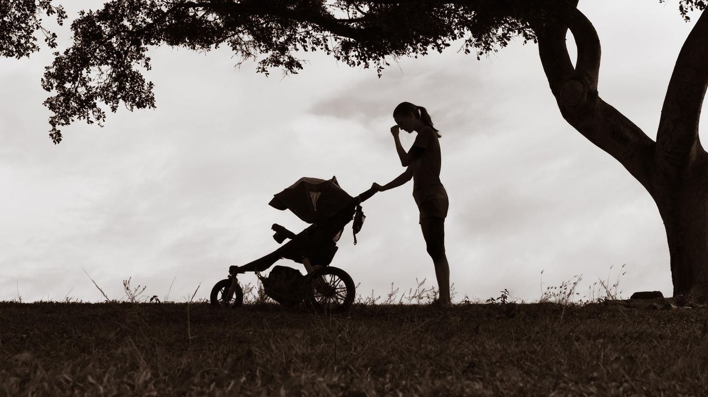 Burnout Mütter Eine Frau steht verzweifelt mit einem Kinderwagen unter einem Baum