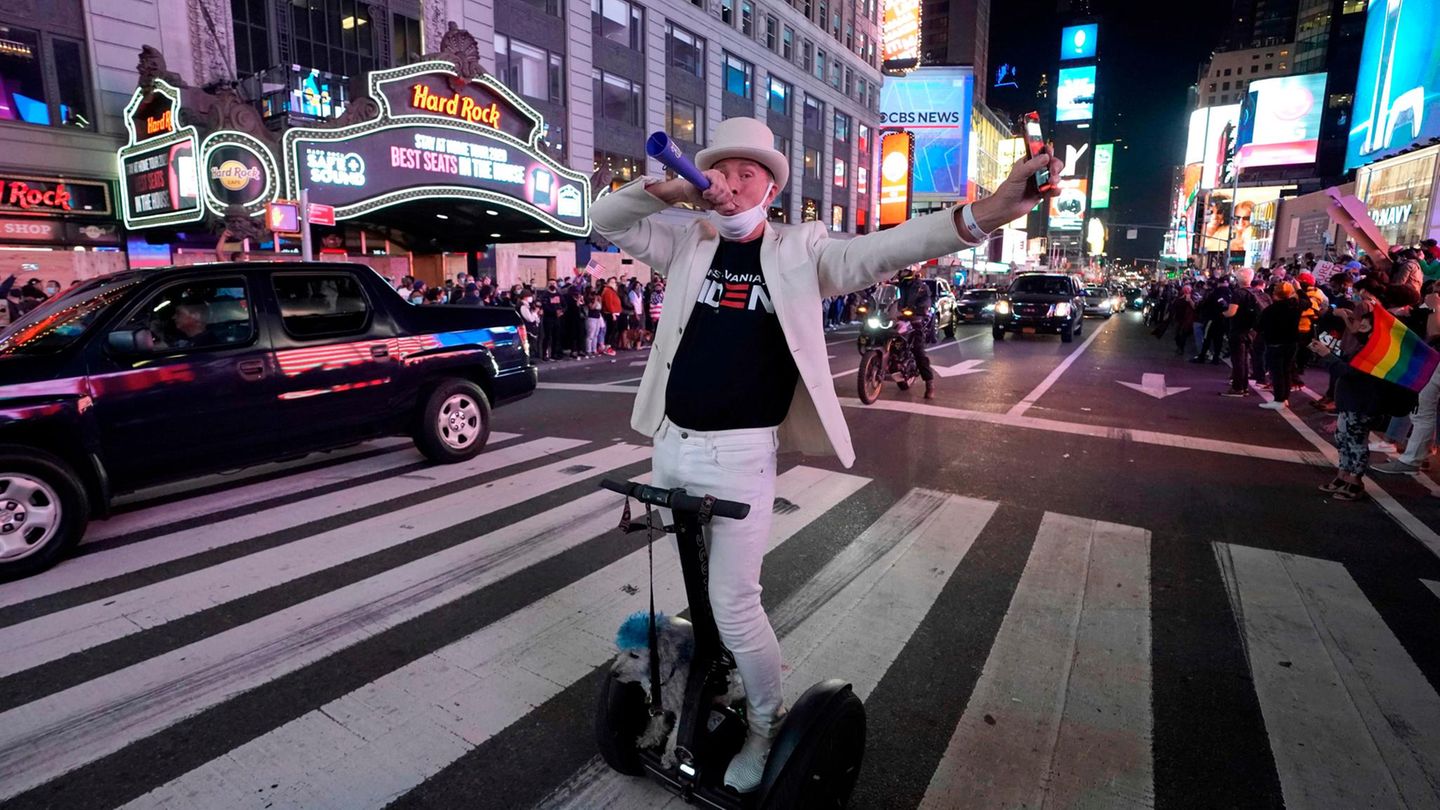 Ein Mann in weißem Anzug auf einem E-Roller bläst in eine Tröte