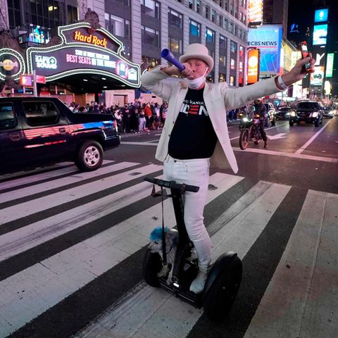 Ein Mann in weißem Anzug auf einem E-Roller bläst in eine Tröte