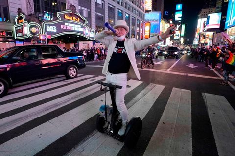 Ein Mann in weißem Anzug auf einem E-Roller bläst in eine Tröte