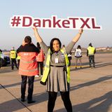 Auf dem Vorfeld hält eine Frau ein Schild mit dem Hashtag "Danke-TXL" in die Luft, während im Hintergrund Hubschrauber der Bundespolizei zum Abschied vorbeifliegen.