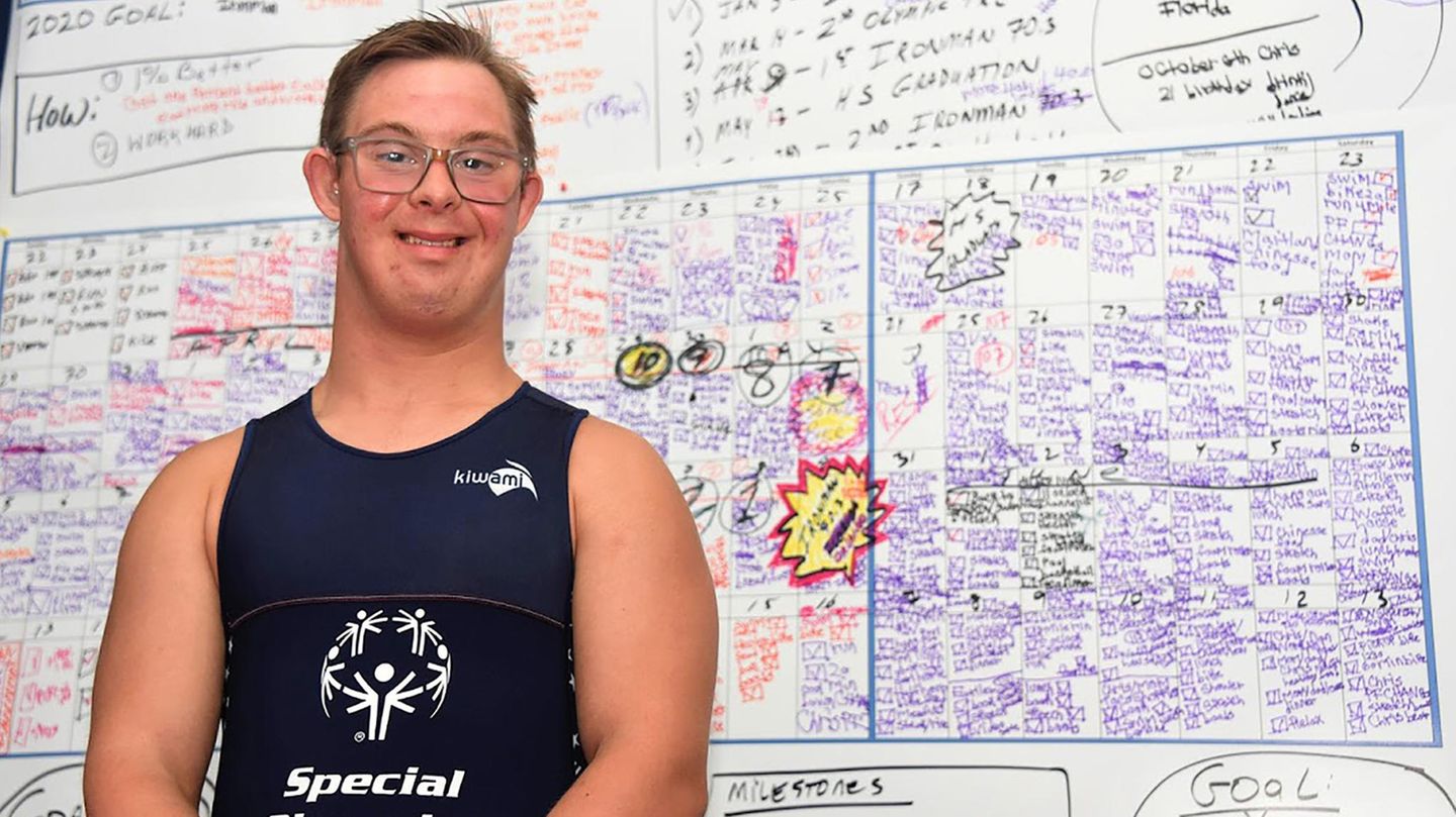 Chris Nikic is in his room in front of a blackboard on which he has his training units listed