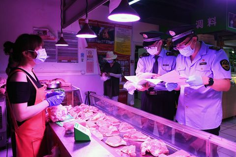 Mitarbeiter der Marktregulierungsverwaltung überprüfen in Peking das Fleisch an einem Marktstand