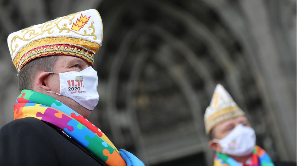 Köln Karneval Vor dem Portal des Kölner Doms ist ein Mann mit Karnevals-Hut im Profil zu sehen. Der Mann trägt Mund-Nasen-Schutz
