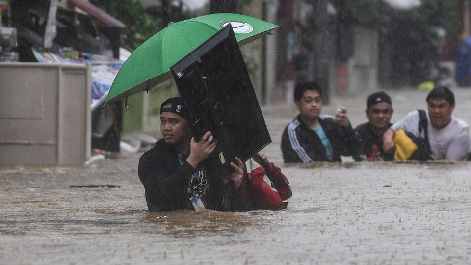 Heftige Überschwemmungen auf den Philippinen: Ein Mann will sich und seinen Fernseher ins Trockene zu bringen.