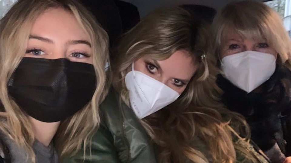 Vor einem dunklen Hintergrund sitzen drei Frauen mit weißen Masken: Leni Klum links, Heidi Klum in der Mitte und Erna rechts