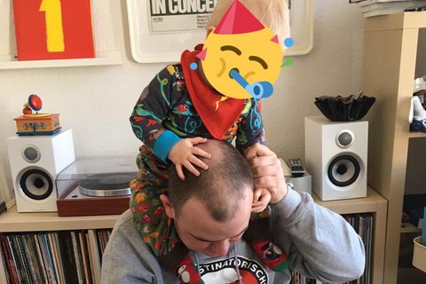 Zeichner Tobias Vogel sitzt am Laptop und hat seinen Sohn auf den Schultern